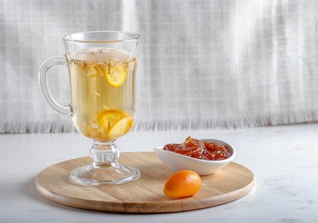Jasmine tea with kumquat in a glass cup on a wooden board on a white background. close up, copy