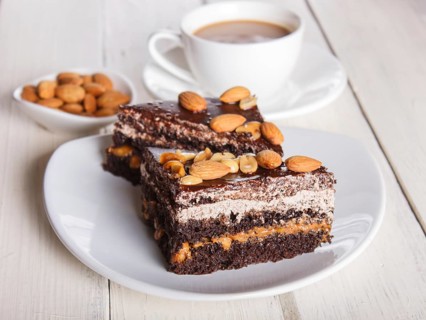Chocolate cake with caramel, peanuts and almonds on a white wooden background. cup of coffee, top