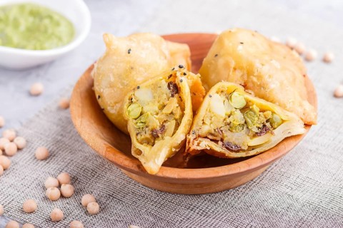 Traditional indian food samosa in wooden plate with mint chutney on a gray concrete background.