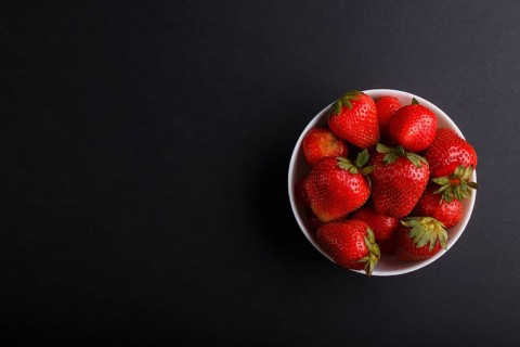 Fresh red strawberry in white bowl on black background. top view, flat lay, copy space