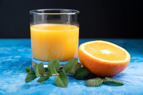 Glass of orange juice with mint on a black and blue background. Hard light, contrast. Side view,