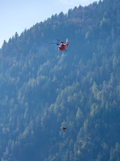 Injured person in a mountain bag with an air rescuer being winched into the rescue helicopter