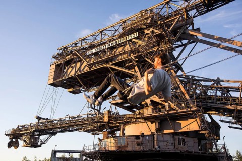 A man swings in front of an open-cast mining excavator illuminated by the evening sun at the Melt