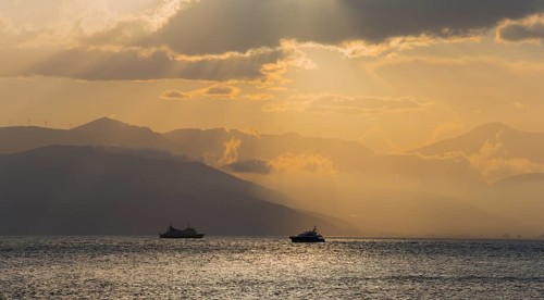 Dramatic sunset over the sea with boat silhouettes and cloudy sky, Agia Kyriaki, Nafplio, Nauplia,