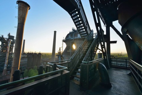 Industrial ruin at sunrise with stairs, metal structures and pipes, flooded with warm sunlight,