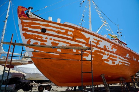 A wooden boat is being restored in dry dock, with the orange and white colour being renewed, Patmos