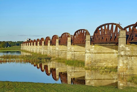 Close-up of stone bridge pillars and the calm water below reflecting the bridge on a clear day,