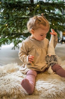 A toddler plays with a Christmas elf in front of a decorated tree