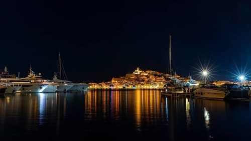 Luxury yachts anchoring in the harbour, behind the illuminated fortress and the old town, night