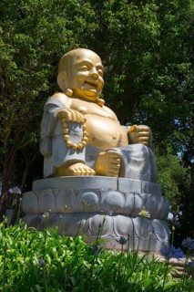 Golden seated Buddha statue in the greenery, surrounded by flowers and trees, radiates peace and