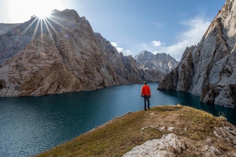 Tourist at the blue mountain lake between rocky steep mountain peaks, Sun Star, Kol Suu Lake,