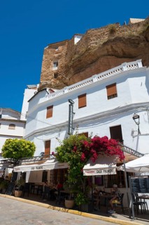 White buildings and restaurant in Setenil de las Bodegas under rocks, blue sky, cave dwellings,