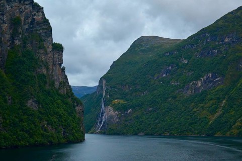 A fjord surrounded by rocky mountains under a cloudy sky with a waterfall in the background,