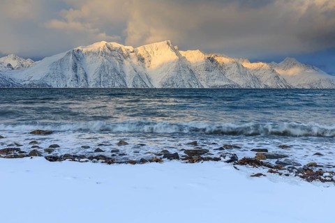 Snow-covered coast and mountains in the morning light, cloudy mood, sea, waves, Lyngen Alps,