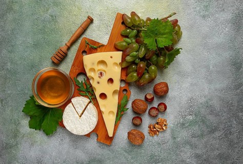 Cheese with big holes, emmental, maasdam, brie cheese, on a cutting board, with grapes and honey,