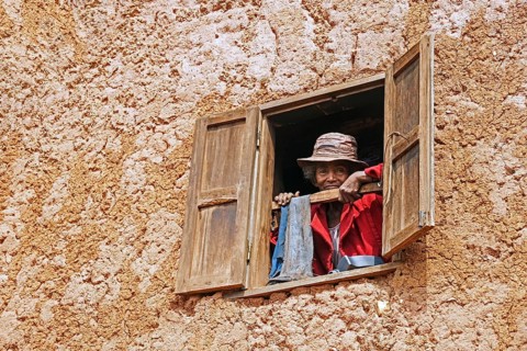 Elderly Malagasy woman looking from window in two stories mud house in the Ambositra District,