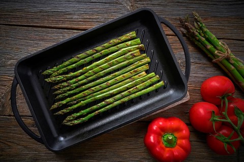 Asparagus grilled on cast iron grill pan on wood table with tomatoes and pepper