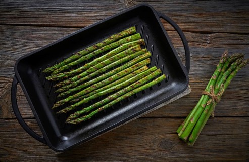 Asparagus grilled on cast iron grill pan on wood table with tomatoes and pepper