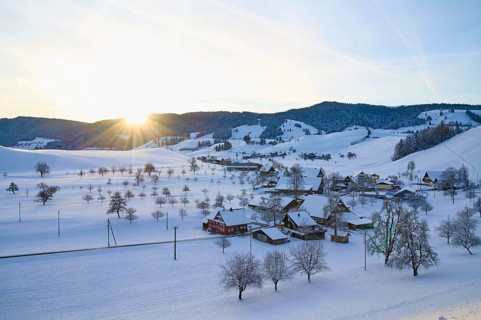 Snow-covered village in winter landscape at sunrise, surrounded by rolling hills, Menzingen, Zug,