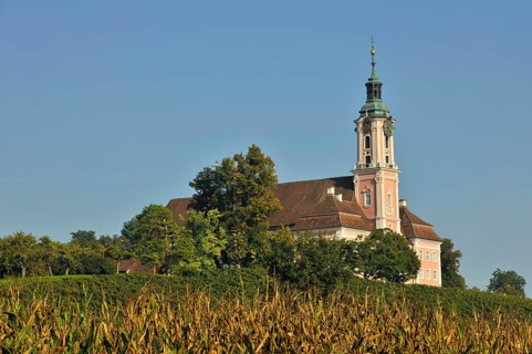 Baroque church stands majestically in the midst of a green landscape under a clear blue sky,