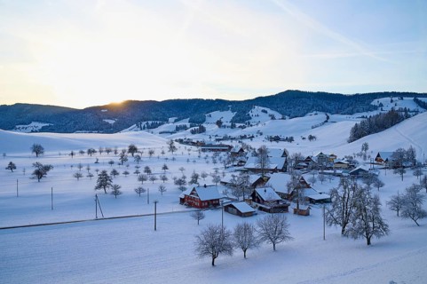 Snow-covered village in winter landscape at sunrise, surrounded by rolling hills, Menzingen, Zug,