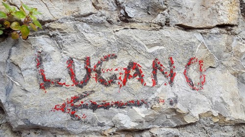 Hand painted red sign on a rock indicating the direction to Lugano, Switzerland, on Sentiero delle