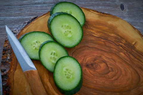 Cucumber slices in and olive wood board with knife