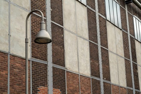 Metal street lamp illuminating an old industrial building facade with brick and concrete walls
