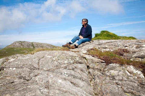Middle aged female hiker sitting high on rocky outcrop in Barra, Outer Hebrides, Scotland, UK