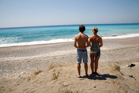 Model released brother and sister twins stand on sandy beach looking out to sea, Rhodes, Greece,