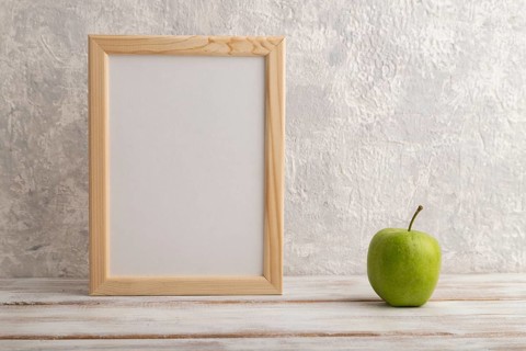 White wooden frame mockup with green apple on gray concrete background. Blank, vertical