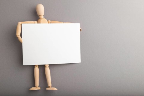 Wooden mannequin holding blank poster on gray pastel background. copy space, isolated, presentation