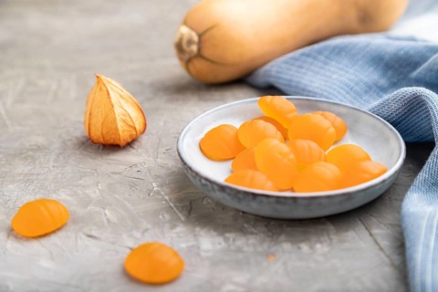 Jelly pumpkin candies on gray concrete background and blue linen textile. close up, side view,