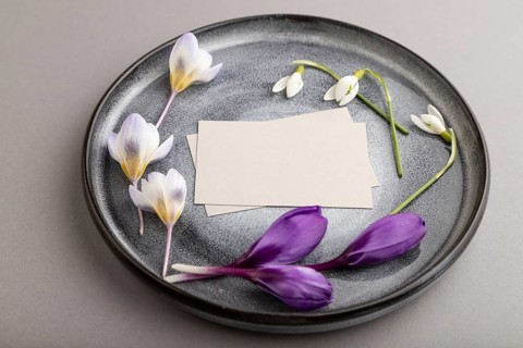 Gray paper invitation card, mockup with crocus and galanthus flowers on ceramic plate and gray