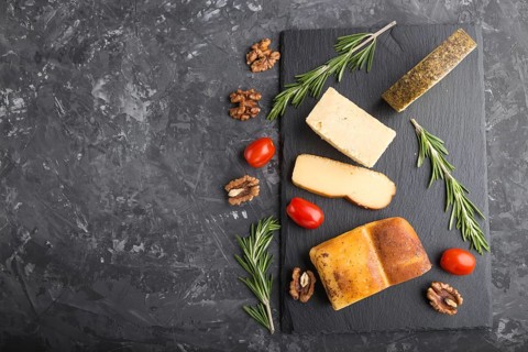 Smoked cheese and various types of cheese with rosemary and tomatoes on black slate board on a
