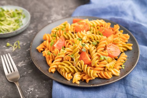 Tortiglioni semolina pasta with tomato and microgreen sprouts on a black concrete background and