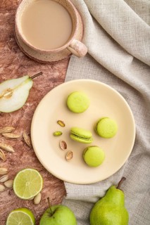 Green macarons or macaroons cakes with cup of coffee on a brown concrete background and linen