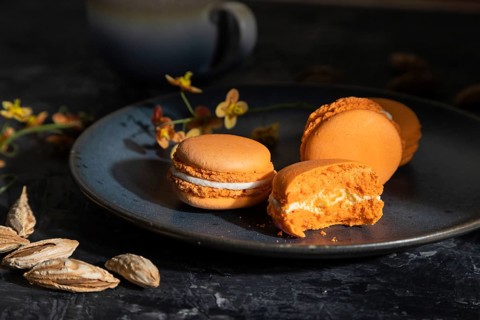 Orange macarons or macaroons cakes with cup of coffee on a black concrete background. Hard light,