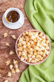 Popcorn with caramel in ceramic bowl on brown concrete background and green textile. Top view, flat