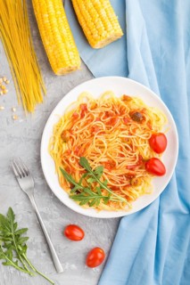 Corn noodles with tomato sauce and arugula on a gray concrete background and blue textile. Top