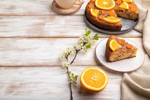 Orange cake and a cup of coffee on a white wooden background and linen textile. Side view, copy