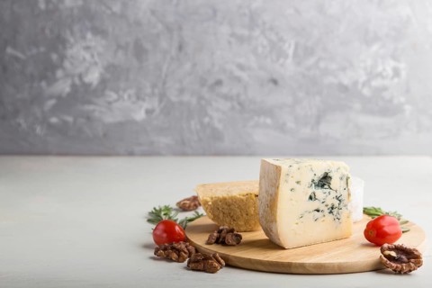 Blue cheese and various types of cheese with rosemary and tomatoes on wooden board on a white and