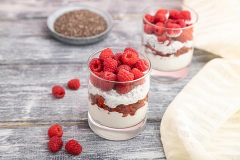 Yogurt with raspberry, goji berries and chia seeds in glass on gray wooden background and linen