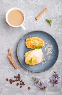 Cheese pancakes on a blue ceramic plate and a cup of coffee on a gray concrete background. top