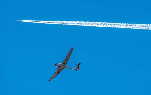 Twin-engine jet, passenger aircraft, with contrails, in the sky, below a motorised sailplane