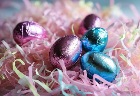 Small chocolate Easter eggs wrapped in shiny foil, placed on a bed of shredded pastel-colored