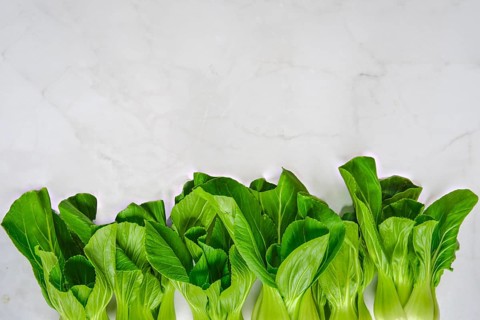 A vibrant display of fresh bok choy sits neatly aligned on a marble countertop. The greens shine