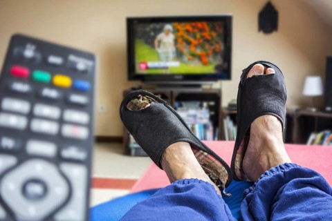 Remote control and couch potato, lazy man in comfy chair wearing worn slippers with big toes