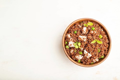 Quinoa porridge with green pea and chicken in wooden bowl on a white wooden background. Top view,