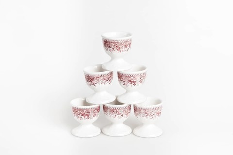 Symmetrically stacked ceramic egg cups with a reddish pattern on a white background